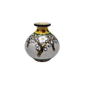 May include: A small, round ceramic vase with a narrow neck and a wide body. The vase is painted with a light gray background and features a design of white flowers and brown branches. The top of the vase is yellow with brown accents.