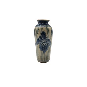 May include: A ceramic vase with a narrow neck and a rounded body, featuring a cream-colored base glaze with hand-painted dark blue floral motifs and vertical brushstrokes that extend from the rim down to the base of the vessel.