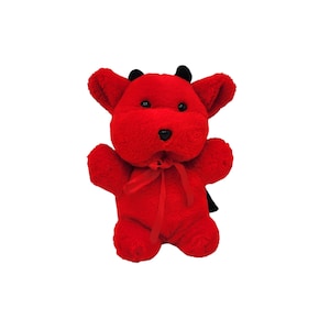 May include: A plush red devil toy with black horns and a black nose. The toy has a red ribbon tied around its neck and outstretched arms. The toy is made of soft, fuzzy material.