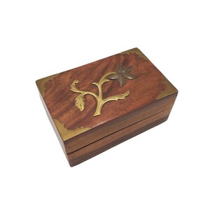 May include: A wooden box with a brass floral design on the lid. The box is made of dark wood and has a brass trim around the edges.