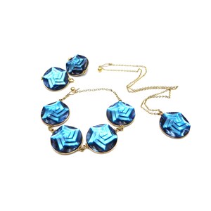 May include: A jewelry set featuring a necklace, bracelet, and earrings. The set includes a gold-toned chain and settings, with faceted blue gemstone pendants. The earrings and necklace have a matching design.
