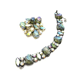 May include: A set of iridescent green and clear rhinestone jewelry featuring a brooch and a bracelet.