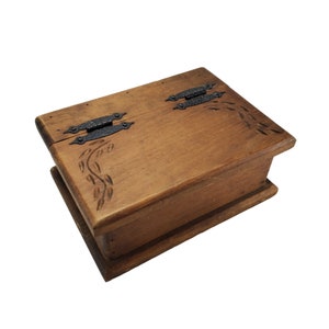 May include: A wooden box with a hinged lid and carved leaf designs. The box has two black metal hinges.