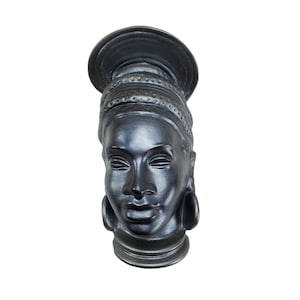 May include: Black ceramic sculpture of a woman's head with a traditional headdress and large earrings.