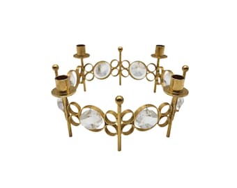 May include: A gold-colored metal candle holder with a circular design. The candle holder features six candle holders and clear, round crystal accents. The design is symmetrical and decorative, suitable for home decor.