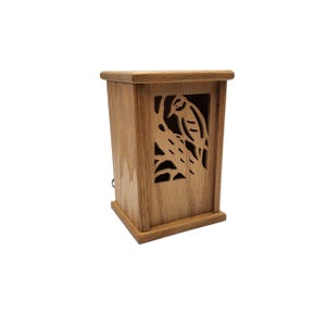 Op de afbeelding: Een rechthoekige houten kist met een uitgesneden vogelontwerp. De kist heeft een lichtbruine afwerking. De vogel zit op een tak en het ontwerp is uit het voorpaneel gesneden. Eenvoudig, elegant ontwerp.