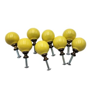 May include: A collection of nine yellow ceramic cabinet knobs with brass-colored bases and silver screws. The knobs are spherical and evenly spaced, with a glossy finish. The hardware is suitable for furniture restoration or DIY projects.
