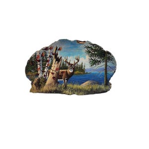 May include: A rustic, hand-painted wooden plaque featuring a serene landscape with a deer standing near a lake. The artwork includes trees, foliage, and a blue sky. The text "LUCAS 1857" is visible on the lower left side of the plaque.
