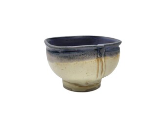May include: Handmade ceramic bowl with a unique design. The bowl features a dark blue rim, a cream-colored center, and a light brown base. The exterior has a textured appearance, adding to its rustic charm. This bowl is perfect for serving soups, salads, or other dishes.