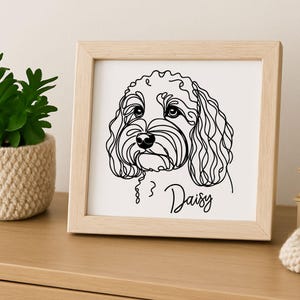 Może przedstawiać: Oprawiony wydruk z czarnym rysunkiem linii przedstawiającym pysk psa, z imieniem "Daisy" w kursywie poniżej. Grafika jest umieszczona w jasnej drewnianej ramie.