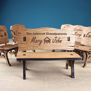 Può includere: Panchina e sedie in miniatura di legno con nomi e testo incisi. La panchina recita "The Johnson Grandparents Mary John" con un simbolo di cuore e casa. Le sedie sono incise con nomi come "Grandpa John" e "Grandma Emma".