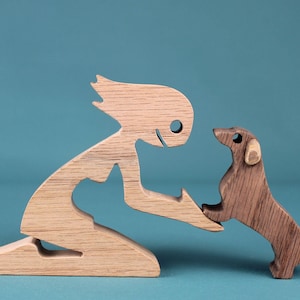 May include: Wooden sculpture of a person and a dog. The person is kneeling, reaching out to the dog. The dog is standing on its hind legs, paws touching the person's hand. The sculpture is made of light and dark brown wood.