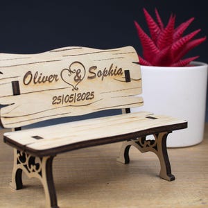 Könnte beinhalten: Eine Holzbank mit einem geschnitzten Herzen und den Namen Oliver & Sophia sowie dem Datum 25.05.2025. Die Bank ist hellbraun und hat einen rustikalen Look.