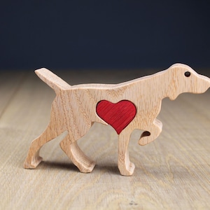 Op de afbeelding: Een houten hondenfiguur met een rood hart in het midden. De hond is gemaakt van lichtkleurig hout met zichtbare houtnerf. Het hart is rood. De hond staat in een wandelhouding, met poten en staart zichtbaar.