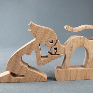 May include: Wooden sculpture of a person kneeling and petting a cat. The sculpture is made of light brown wood and has a simple, stylized design.