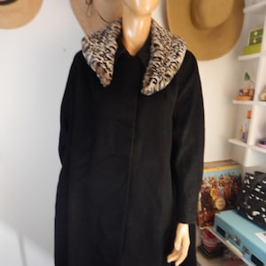 May include: A long, black coat with a leopard print collar. The coat is displayed on a mannequin. The coat has a classic design and appears to be made of a heavy material, suitable for cold weather.