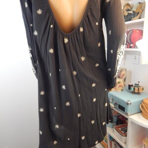 May include: A dark gray dress with long sleeves and a low back. The dress is adorned with small, white floral embroidery scattered across the fabric. The sleeves also feature white embroidery near the cuffs. The dress has a loose, flowing silhouette.