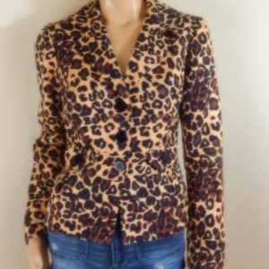 May include: A tan blazer with a brown and black leopard print pattern. The blazer has a notched collar, long sleeves, and black buttons. The model is wearing blue denim shorts.