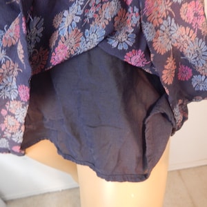 May include: A navy blue top with a floral pattern in shades of pink, blue, and peach. The top has a sheer outer layer and a solid navy blue lining. The floral design is concentrated around the edges of the top.