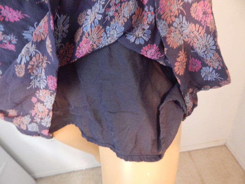 May include: A navy blue top with a floral pattern in shades of pink, blue, and peach. The top has a sheer outer layer and a solid navy blue lining. The floral design is concentrated around the edges of the top.