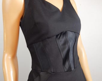 May include: A sleeveless black dress with a V-neckline and a fitted bodice. The bodice features vertical paneling, creating a corset-like appearance. The dress has a tailored, streamlined silhouette.