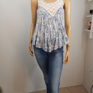 May include: A sleeveless blue and white floral print top with a crochet neckline and a tiered ruffle hem. The top is paired with blue denim jeans.