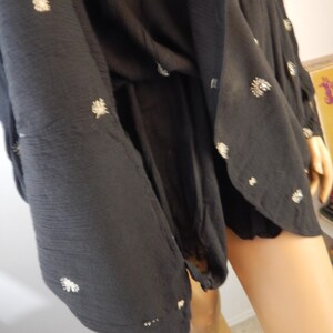 May include: Black dress with white floral embroidery. The dress has long sleeves and a flowing silhouette. The fabric appears to be a lightweight material, suitable for warmer weather. The dress is shown on a mannequin.