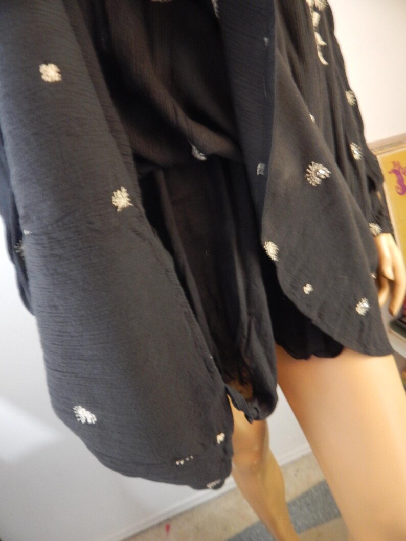 May include: Black dress with white floral embroidery. The dress has long sleeves and a flowing silhouette. The fabric appears to be a lightweight material, suitable for warmer weather. The dress is shown on a mannequin.