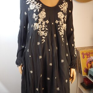 May include: Black long-sleeve dress with a scoop neck and floral embroidery. The dress features white embroidered flowers and small white floral accents. The dress is made of a lightweight fabric and has a loose, flowing fit.