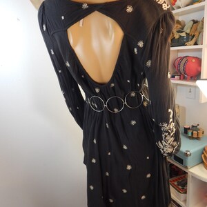 May include: Black dress with long sleeves and a keyhole back. The dress features white floral embroidery and a silver belt. The dress is displayed on a mannequin.