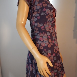 May include: A dark purple dress with a floral pattern in pink, blue, and orange. The dress has short, ruffled sleeves and a V-neckline with a tie. The fabric appears lightweight and flowing, suitable for warm weather.