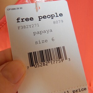 Puede incluir: Una etiqueta blanca de Free People con la palabra "papaya" y la talla "6". La etiqueta tambi&eacute;n incluye un c&oacute;digo de barras y la frase "suggested retail price". La etiqueta est&aacute; sujeta a una prenda de color papaya.