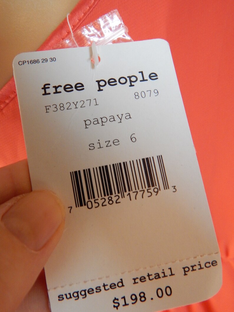 Puede incluir: Una etiqueta blanca de Free People con la palabra "papaya" y la talla "6". La etiqueta tambi&eacute;n incluye un c&oacute;digo de barras y la frase "suggested retail price". La etiqueta est&aacute; sujeta a una prenda de color papaya.