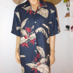 May include: Navy blue short-sleeve shirt with a tropical leaf pattern in beige and red. The shirt has a button-down front and a collared neckline. The fabric appears to be a lightweight material, suitable for warm weather.