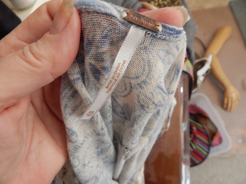 May include: Close-up of a light-colored top with a blue tie-dye pattern. The tag reads "Free People" and "Made in China / Fabriqu&eacute; en Chine". The fabric appears to be a lightweight knit.
