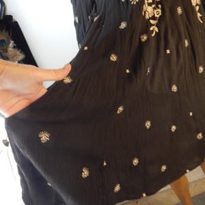 May include: Black dress with embroidered floral and dot patterns. The dress features a flowing silhouette and is adorned with intricate, light-colored floral embroidery along the neckline and scattered across the fabric. The dress is made of a lightweight material.