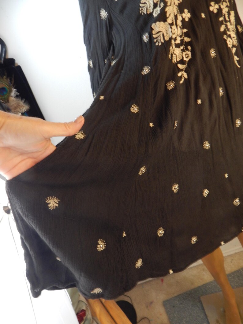May include: Black dress with embroidered floral and dot patterns. The dress features a flowing silhouette and is adorned with intricate, light-colored floral embroidery along the neckline and scattered across the fabric. The dress is made of a lightweight material.
