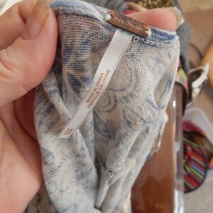 May include: Close-up of a light-colored top with a blue tie-dye pattern. The tag reads "Free People" and "Made in China / Fabriqu&eacute; en Chine". The fabric appears to be a lightweight knit.