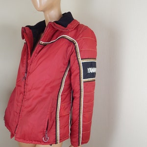 May include: Red and black Yamaha racing jacket with gold and white accents. The jacket has a black collar and a zipper closure. The Yamaha logo is displayed on the sleeve.