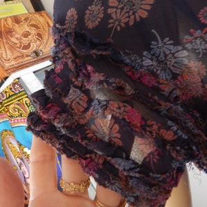May include: Dark navy blue sheer fabric with a floral pattern in shades of pink, orange, and blue. The edge of the fabric has a ruffled trim. The fabric is lightweight and appears to be a blouse or dress material.