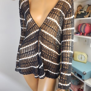 May include: A black and white striped open-weave cardigan with long sleeves. The cardigan has a deep V-neck and a single button closure. The white stripes are horizontal and evenly spaced across the black background. The garment is displayed on a mannequin.