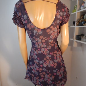 May include: A dark purple dress with a floral pattern in pink, blue, and peach. The dress features a low back with crisscross straps and short, ruffled sleeves. The dress is displayed on a mannequin.