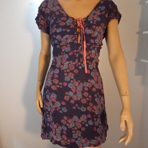 May include: A dark purple floral print dress with a V-neckline and short sleeves. The dress features a tie detail at the bust and a flared skirt. The floral pattern includes pink, orange, and blue flowers. The dress is displayed on a mannequin.
