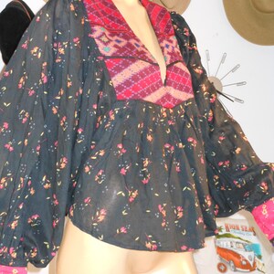 May include: A dark navy blouse with a floral pattern and a deep V-neck. The neckline and cuffs feature a vibrant red and pink geometric design. The sleeves are long and billowy, and the cuffs are a bright pink.