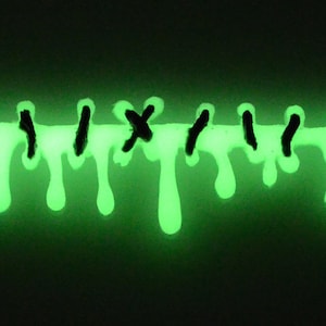 May include: A close-up of green glow-in-the-dark paint dripping down a surface. The paint is in the shape of a line with black X's and vertical lines.