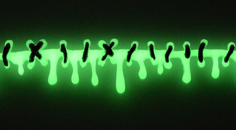 May include: A close-up of green glow-in-the-dark paint dripping down a surface. The paint is in the shape of a line with black X's and vertical lines.