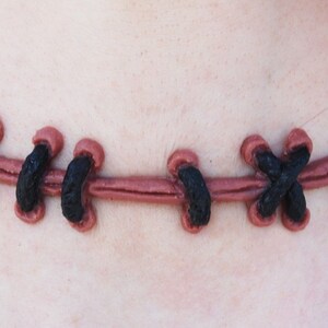 May include: A brown leather choker necklace with black stitching in a criss-cross pattern.