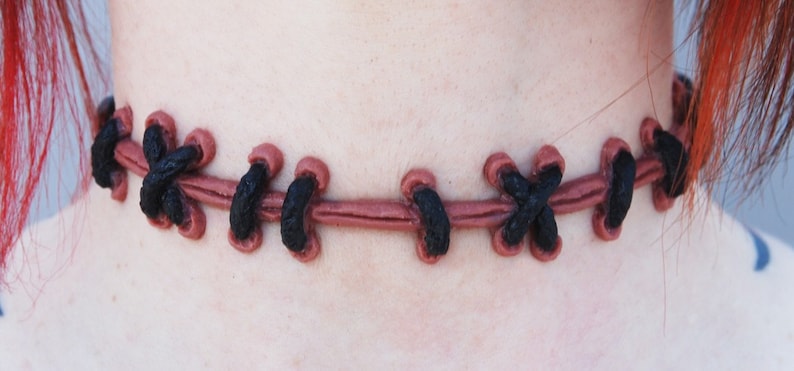 May include: A brown leather choker necklace with black stitching in a criss-cross pattern.