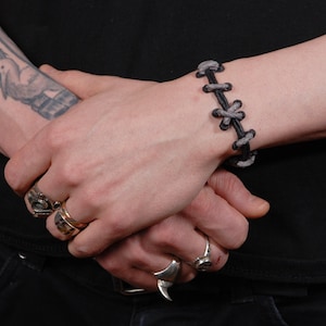 May include: A black leather bracelet with grey stitching and a criss-cross pattern.