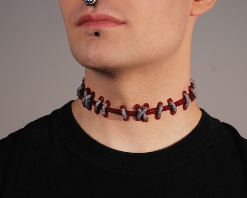 May include: A red and gray choker necklace with a stitched design. The necklace is made of a soft, flexible material and is worn around the neck.